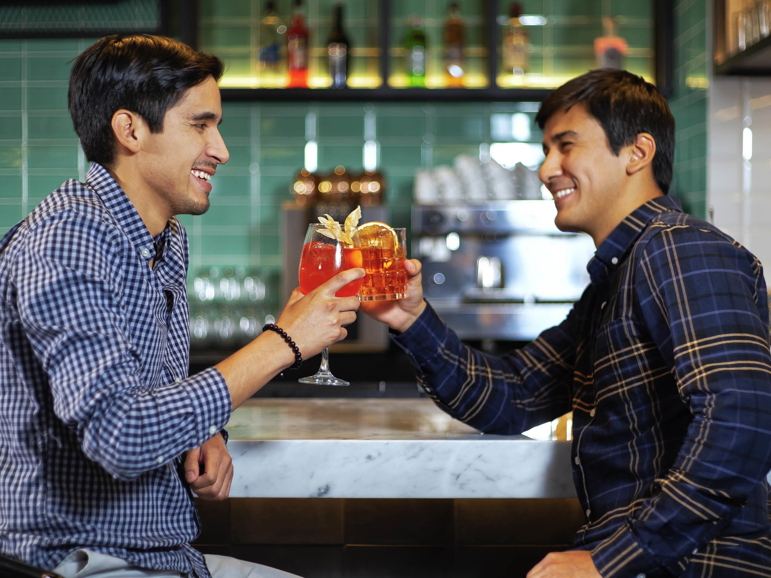 Duas pessoas sentadas em um bar, segurando bebidas com guarnições.