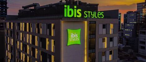 Un edificio con la señalización de 'ibis Styles', que presenta un diseño arquitectónico moderno con una estructura de ventanas y un techo plano.