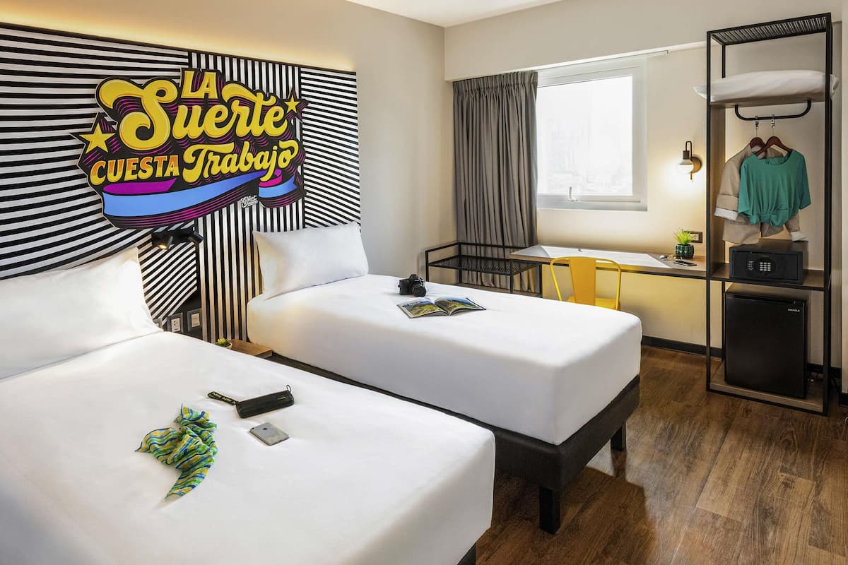 Una habitación de hotel con dos camas, un escritorio, un armario y una ventana con cortinas.