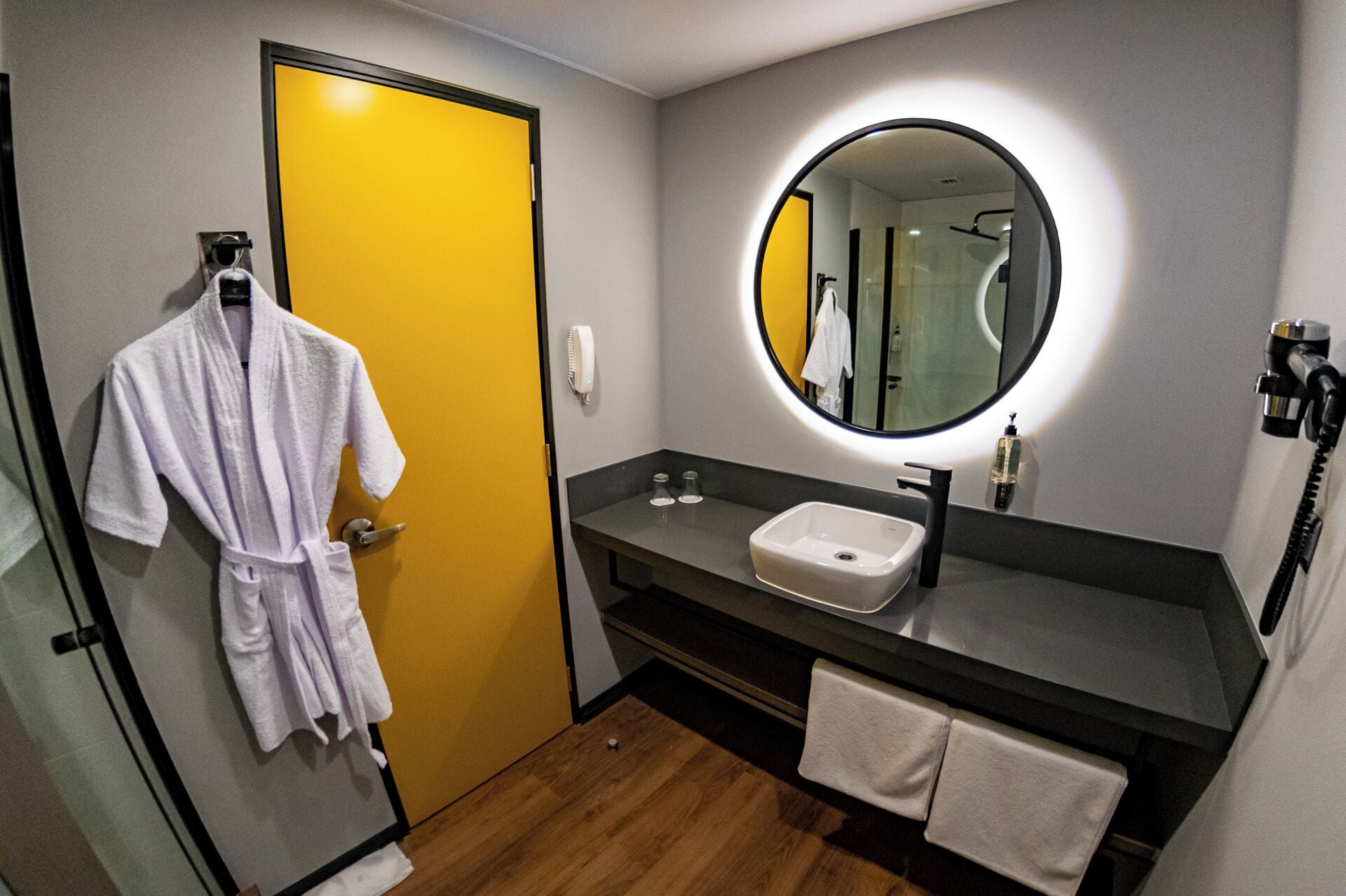 A hotel bathroom with a yellow door, a round mirror, a sink, and a robe rack.