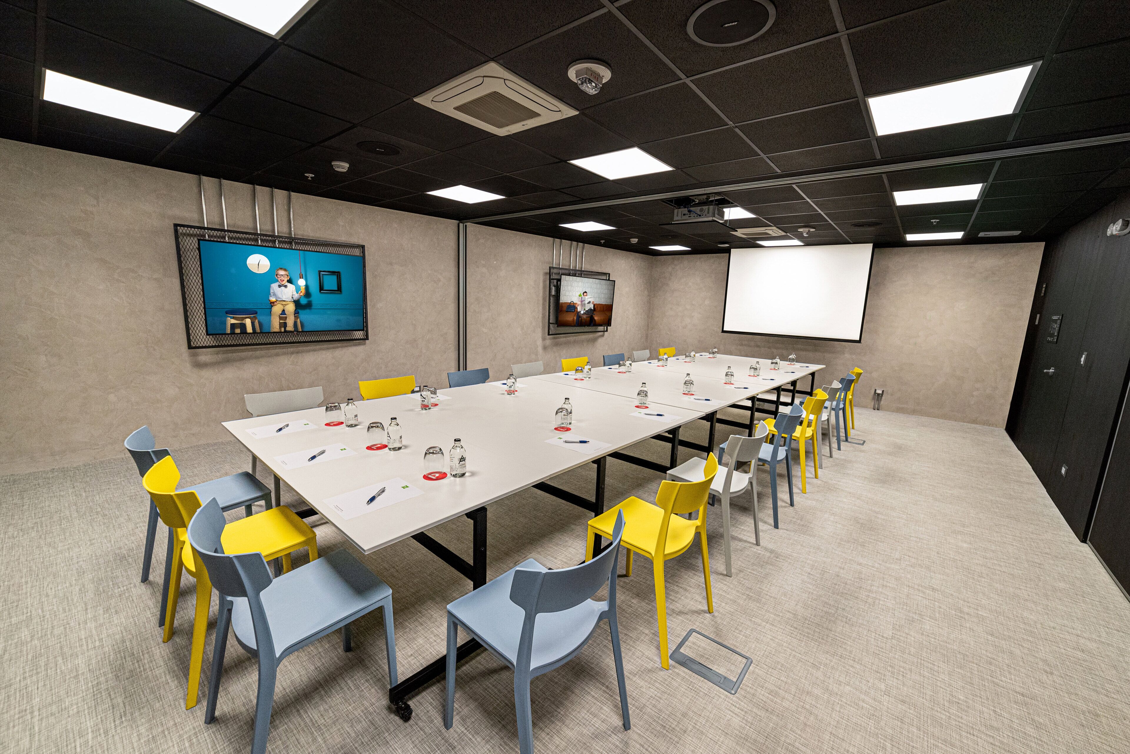 A conference room with a long table, multiple chairs, and a projector screen.