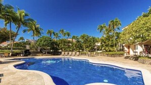 A swimming pool with a curved edge, surrounded by palm trees and lounge chairs. - Comfortable and cozy condo (Waikoloa Village)