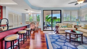 A spacious living area with a bar, seating, and a view of the outdoors. - Comfortable and cozy condo (Waikoloa Village)