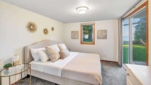 Ein Schlafzimmer mit Bett, Nachttisch und Fenster mit Blick auf Grünflächen.