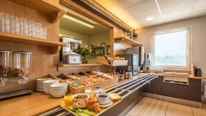 A breakfast buffet with various food items and beverages, a coffee machine, and a window with blinds. - B&B HOTEL Vannes Ouest Golfe du Morbihan (Vannes)