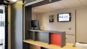 A reception desk with a computer monitor, a printer, and a television screen displaying a welcome message. - B&B HOTEL Vannes Ouest Golfe du Morbihan (Vannes)