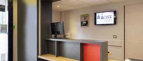 A reception desk with a computer monitor, a printer, and a television screen displaying a welcome message.