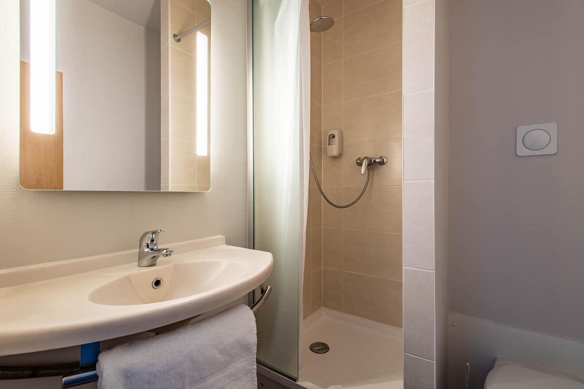A bathroom with a sink, mirror, shower, and a towel.