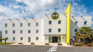 A modern B&B hotel with a bright yellow flag, a sign reading "ACCUEIL," and a clean, white facade with multiple windows. - B&B HOTEL Vannes Ouest Golfe du Morbihan (Vannes)
