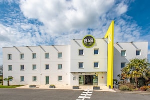 A modern B&B hotel with a bright yellow flag, a sign reading "ACCUEIL," and a clean, white facade with multiple windows.
