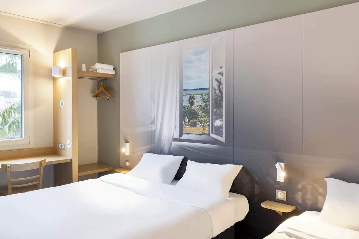A hotel room with a bed, a desk, a chair, a window with a view, and a hanging coat rack.