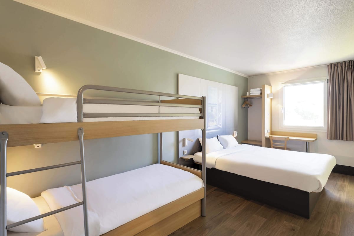 A hotel room with bunk beds, a desk, and a window with curtains.