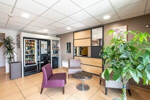 A lobby with seating, vending machines, and a large plant.