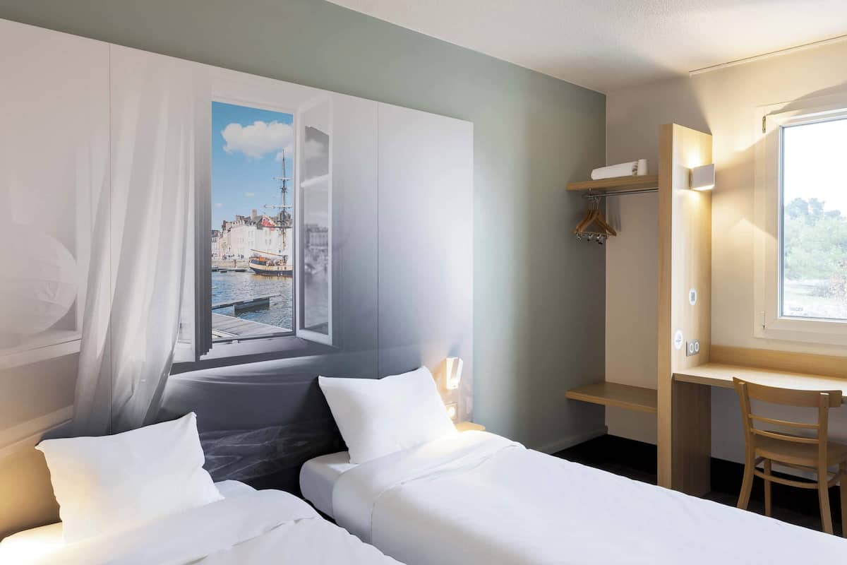 A hotel room with two beds, a desk, and a large window with a view of a cityscape.