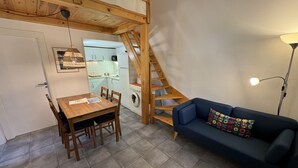 A cozy living area with a wooden dining table, blue sofa, and a staircase leading to a kitchen. - Gregal 81 - A/C, pool and garden (Torroella de Montgri)