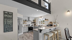 Una cocina moderna con una isla central, taburetes de bar y un cartel con las normas de la casa en la pared.