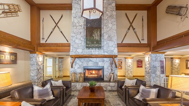 A lobby with stone walls, a fireplace, leather sofas, and skis on the wall.