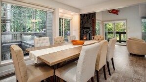 Un espace repas moderne avec une table en bois, des chaises recouvertes d’un tissu beige et une cheminée.