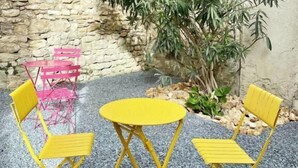Un pequeño espacio al aire libre con pared de piedra, una mesa amarilla y sillas amarillas.