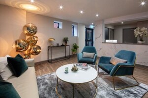 Una sala moderna con una mesa de centro redonda blanca, dos sillones azules, un sofá y espejos esféricos decorativos en la pared.