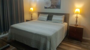 Un lit bien fait, avec deux oreillers, deux lampes de chevet, un ventilateur de plafond et un tableau décoratif au mur.