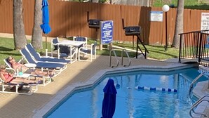 Un espace piscine comprenant des chaises longues, un parasol et un panneau indiquant la présence d’un sauveteur.
