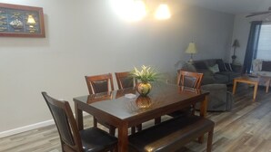 Un coin repas avec une table en bois, des chaises et un banc. On y trouve une lampe et un tableau encadré accroché au mur.