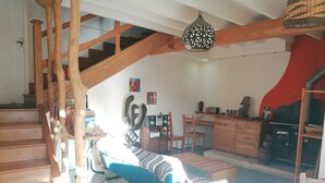 Una escalera de madera que lleva a una sala de estar con un sofá, sillas, una mesa, un radio y una chimenea.