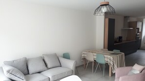 Een moderne woonkamer met een grijze bank, een roze fauteuil en een eethoek met een tafel en stoelen.