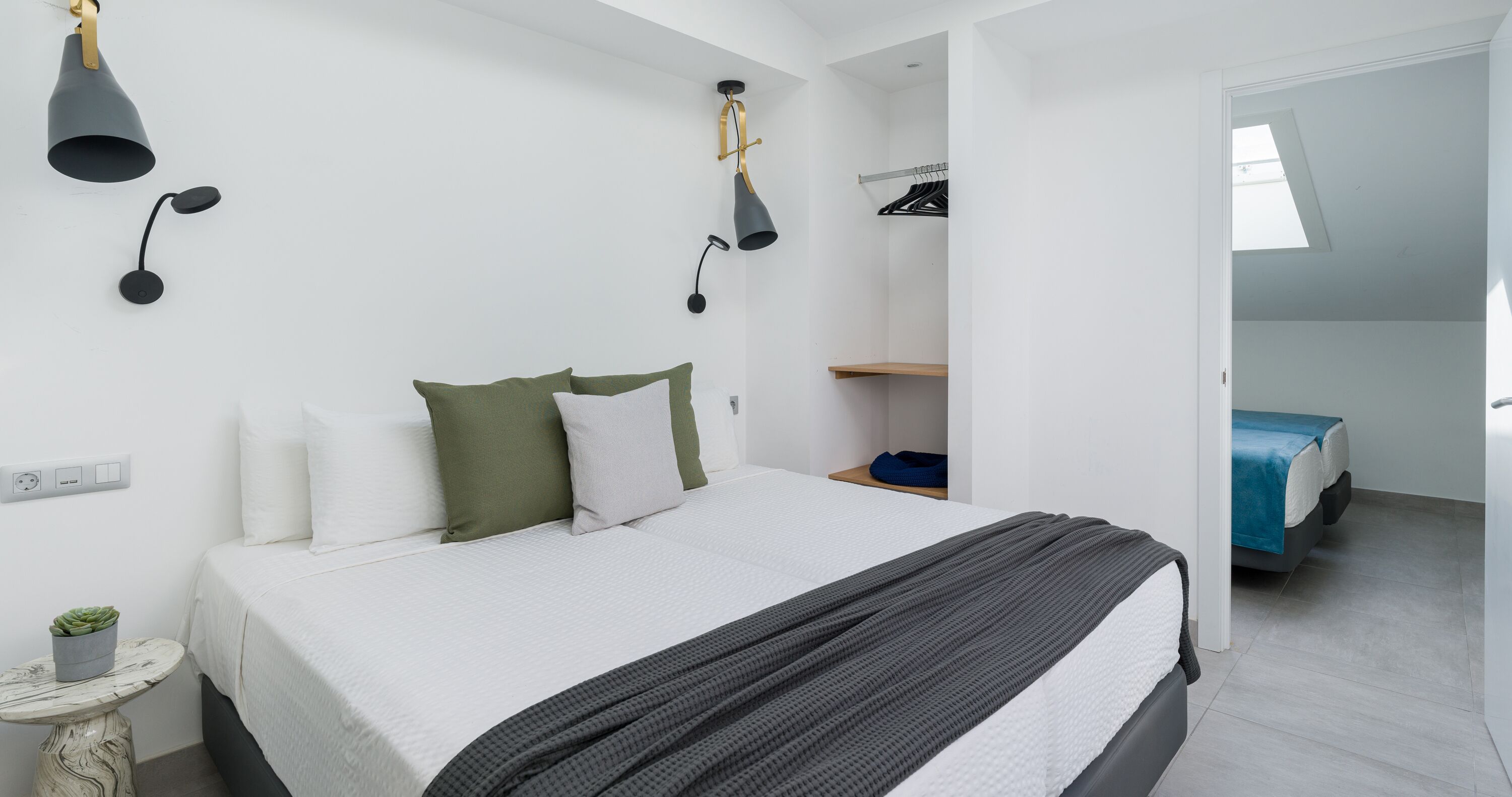 Quarto com cama, mesa de cabeceira, abajur e armário com roupas penduradas.