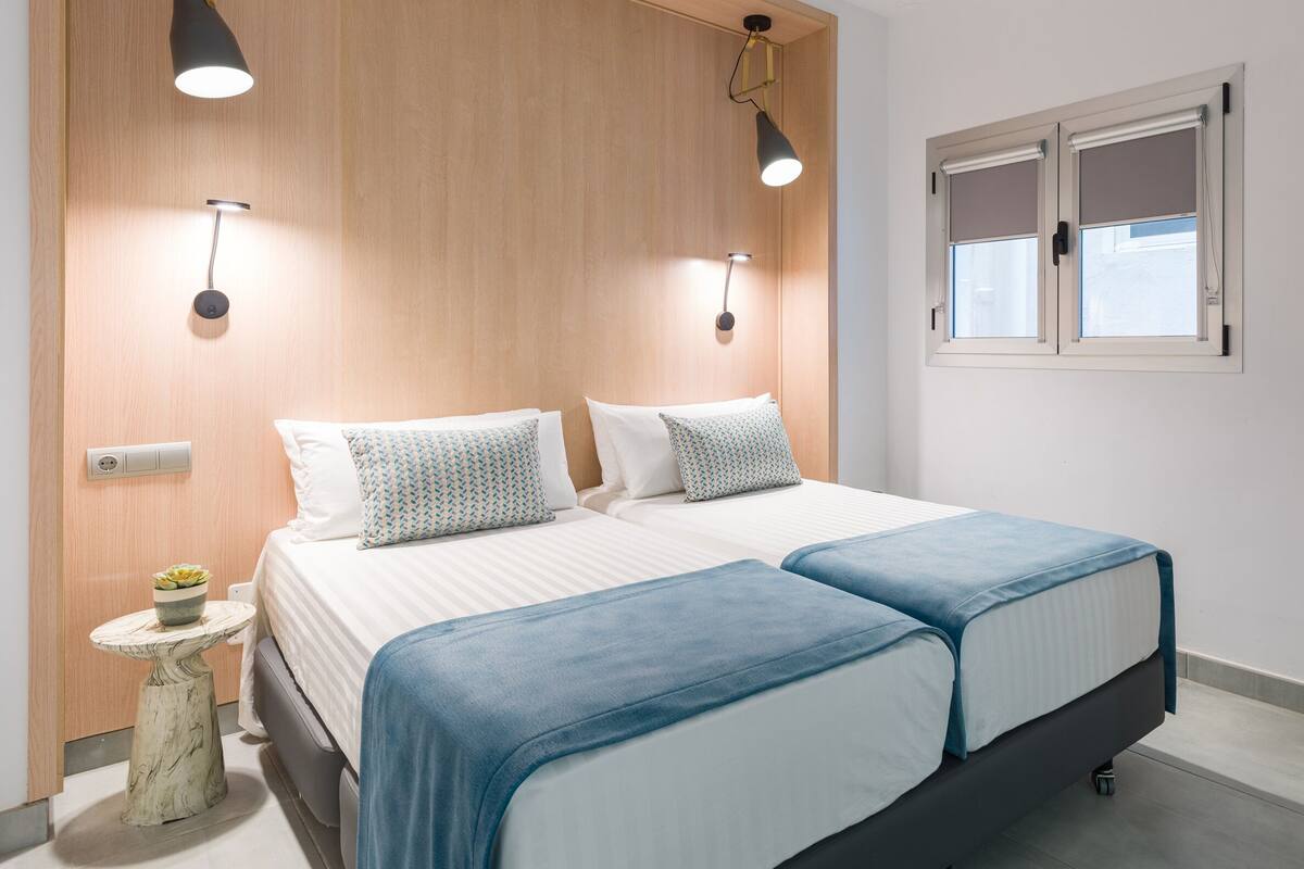 A bedroom with a bed, bedside tables, a small table with a plant, and a window with blinds.