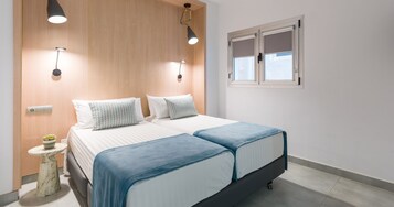 Ένα υπνοδωμάτιο με ένα κρεβάτι, κομοδίνα, ένα μικρό τραπέζι με ένα φυτό και ένα παράθυρο με περσίδες.