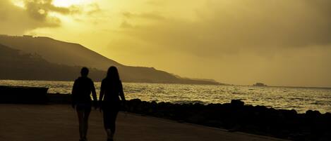 Two people walking on a paved path by the sea during sunset.
