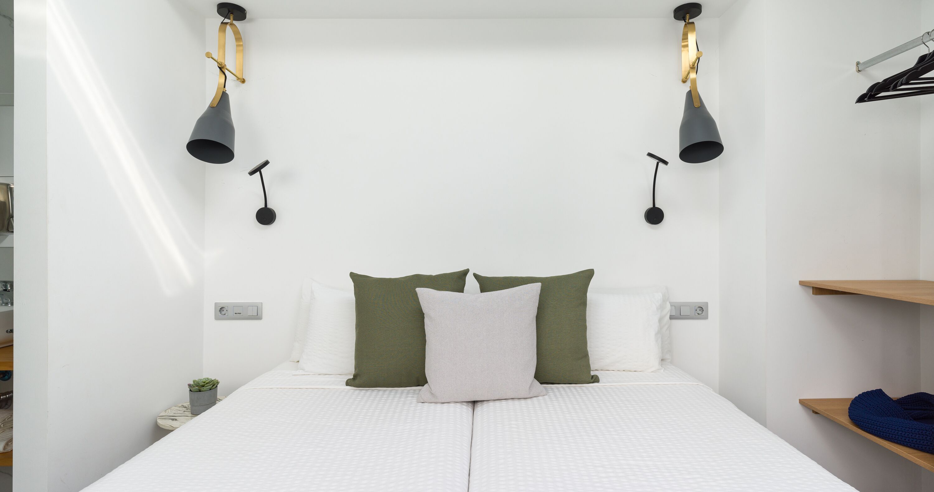 Un dormitorio minimalista con una cama, dos lámparas de pared y un estante con un objeto azul.