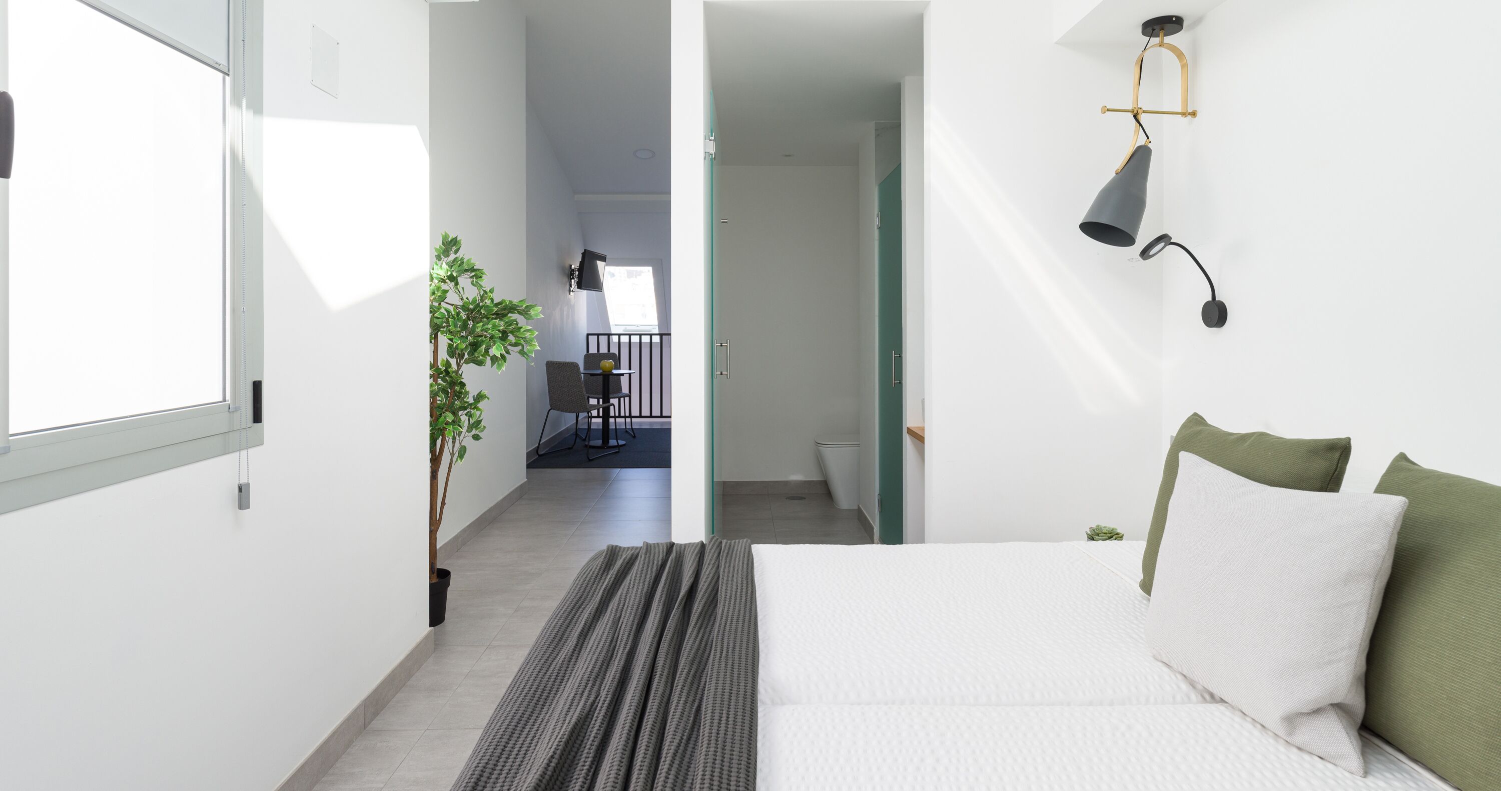Un dormitorio con cama, una planta en maceta, un escritorio con silla y vistas a un balcón.