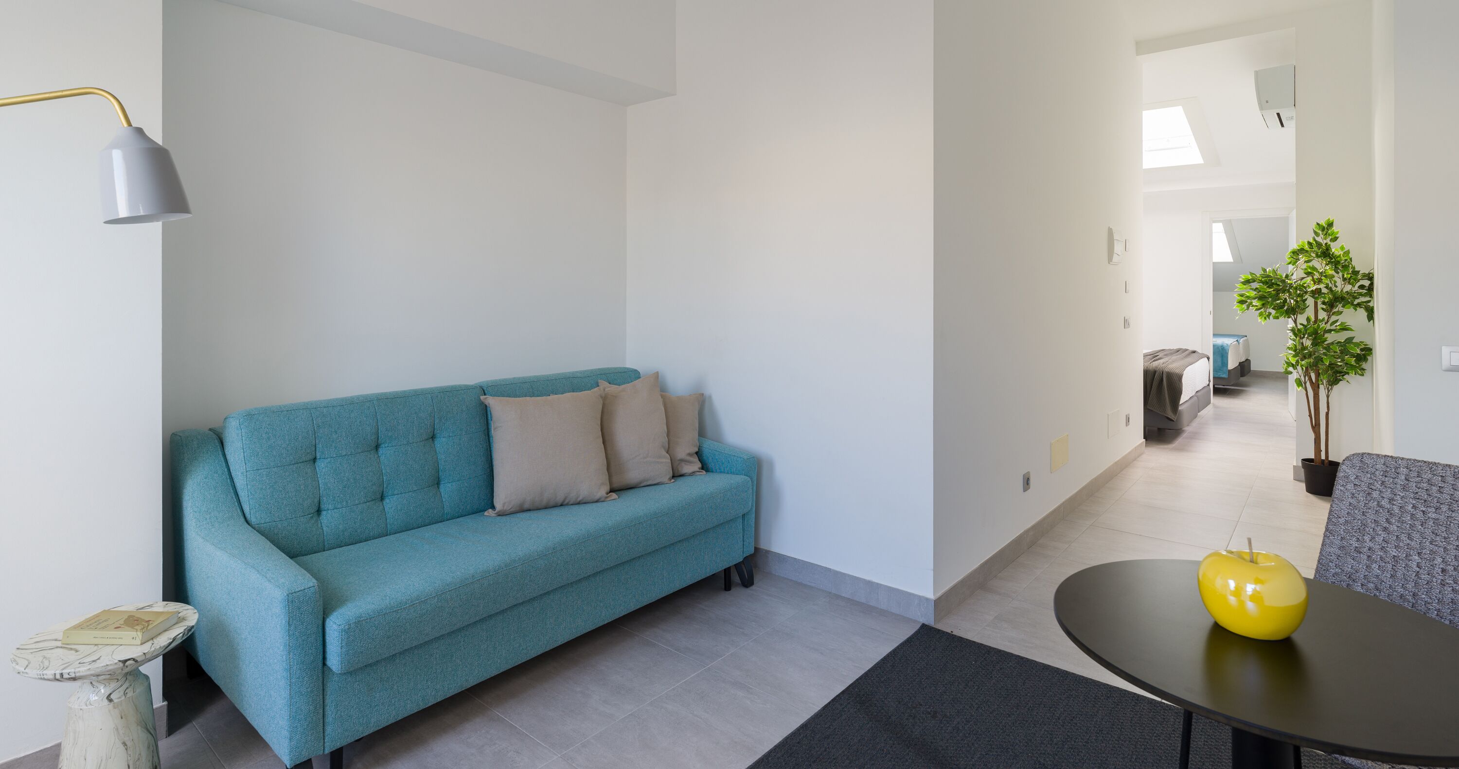 Una sala de estar moderna con un sofá color turquesa, una mesita redonda con un objeto amarillo y una planta en maceta.
