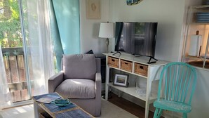 Een woonkamer met een grijze bank, een turquoise fauteuil, een televisie en een lamp.