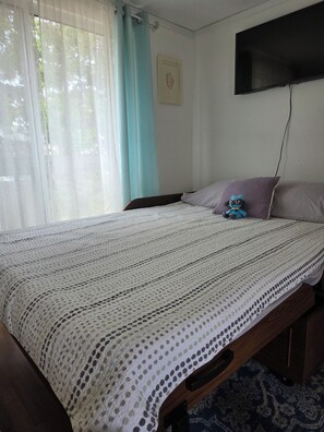 A bedroom with a bed, a television mounted on the wall, and a window with curtains.