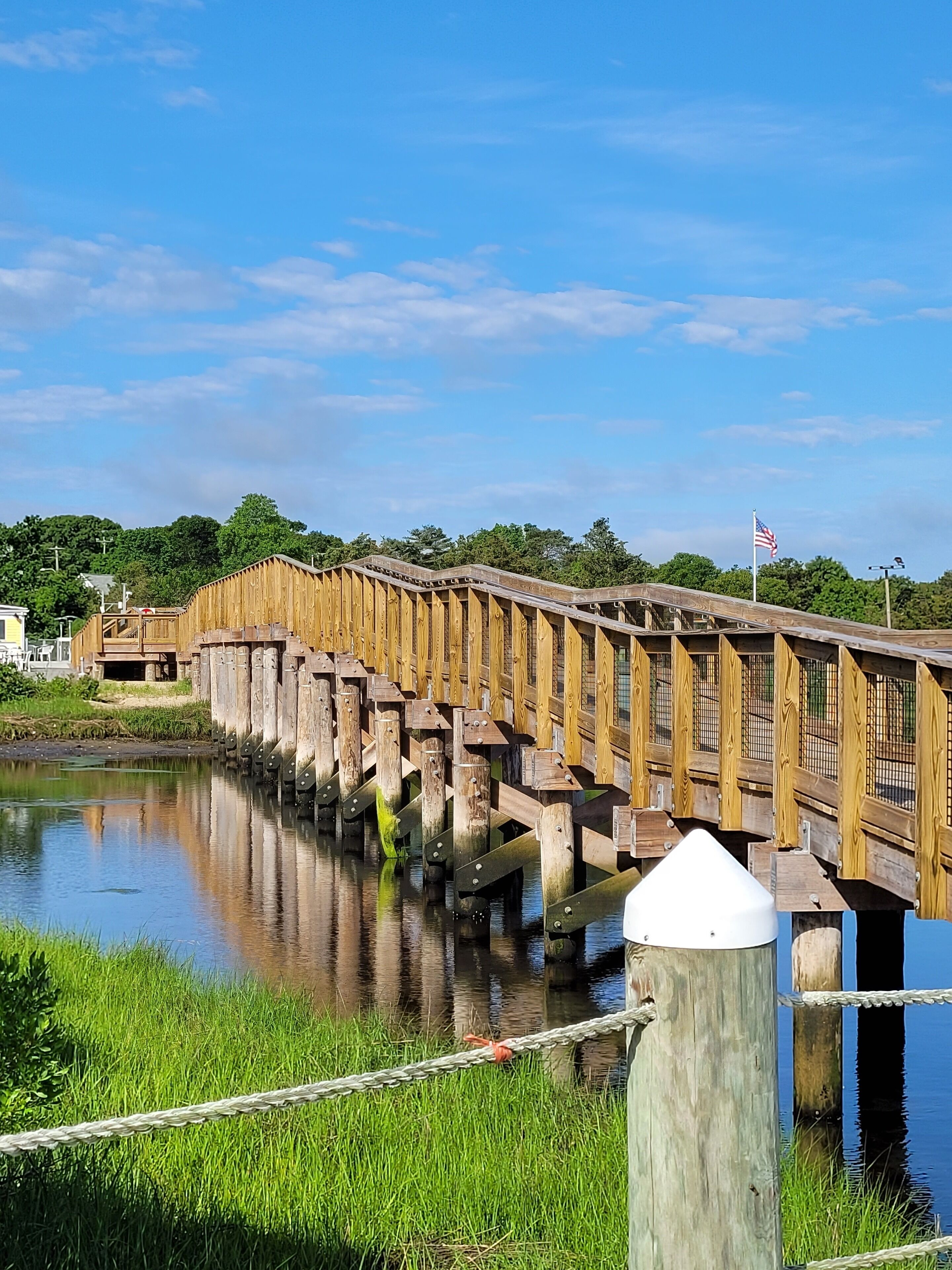 A wooden bridge over a calm river with a grassy bank.