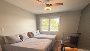 Une chambre avec deux lits, un ventilateur de plafond, une fenêtre avec vue et un plancher en bois.
