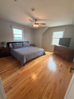 Een slaapkamer met een bed, nachtkastjes, een dressoir, een plafondventilator en twee ramen.