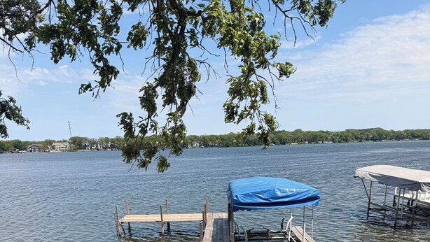 Une jetée en bois s’avançant dans un lac, avec un abri pour bateaux et un arbre qui la surplombe.