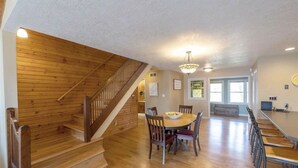 Une salle à manger spacieuse avec un escalier en bois, un lustre et une grande table entourée de chaises.