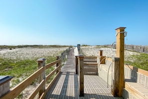 Une promenade en bois mène à une plage de sable, et une structure en bois se trouve sur la droite.