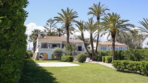 A large, two-story house with a tiled roof, surrounded by well-maintained lawns and palm trees. - 030 Villa Marines (Denia)