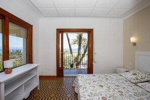 Ein Schlafzimmer mit Bett, Nachttisch, Schreibtisch und Blick aufs Meer durch eine Tür.