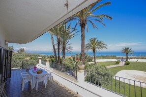 Ein Balkon mit Tisch und Stühlen, der Blick auf einen Strand mit Palmen und einem klaren Himmel bietet.