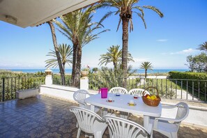 Eine Terrasse mit Tisch für zwei Personen, mit Blick auf einen Strand mit Palmen und einem klaren Himmel.