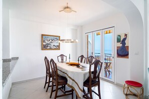 A dining area with a table set for four, wooden chairs, a ceiling fan, and a painting on the wall.