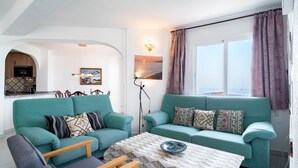 Un salon avec deux canapés de couleur turquoise, une table basse et un coin repas donnant sur une cuisine, séparée par une arche.